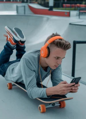 joven-patinador-con-auriculares-naranjas-acostado-en-el-patineta-pensativo-usando-el-telefono-celular-con-patin-moderno copia
